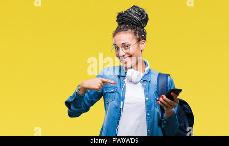 Les jeunes cheveux tressés african american girl étudiant à l'aide de blackberry sur fond isolé avec surprise face à face à lui-même Banque D'Images