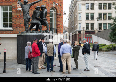 Un London tour guide avec un groupe de touristes américains à l'échelle nationale statue commémorative de pompiers dans Carter Lane Gardens, London, England, UK Banque D'Images