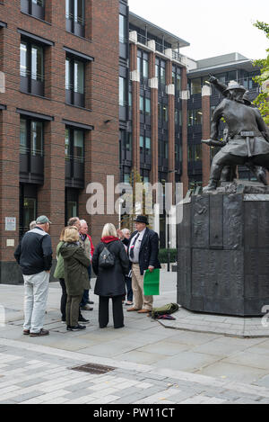 Un London tour guide avec un groupe de touristes américains à l'échelle nationale statue commémorative de pompiers dans Carter Lane Gardens, London, England, UK Banque D'Images