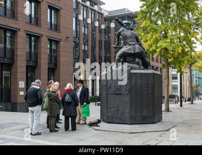 Un London tour guide avec un groupe de touristes américains à l'échelle nationale statue commémorative de pompiers dans Carter Lane Gardens, London, England, UK Banque D'Images