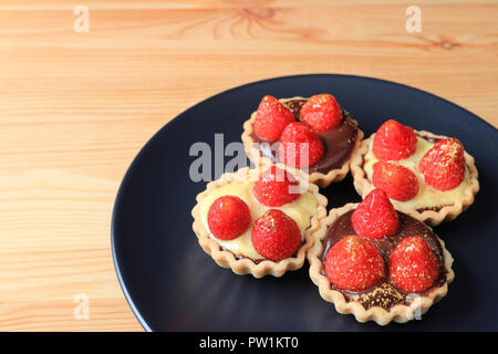 Quatre morceaux de mini tartelettes au chocolat garnie de fraises fraîches et de la poudre d'or comestible servi sur la plaque noire Banque D'Images