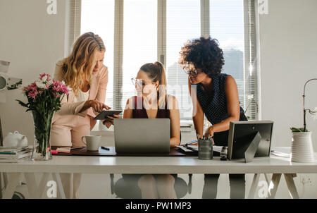 Groupe de jeunes femmes qui travaillent ensemble dans le bureau. Les femmes dans l'emploi temporaire à l'aide d'ordinateur portable et tablette numérique dans un bureau moderne. Banque D'Images