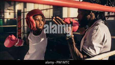 Enseignement formateur un enfant comment toucher les poinçons. Kid boxing et l'entraînement de la garde la tête avec son entraîneur à l'intérieur d'un ring de boxe. Banque D'Images