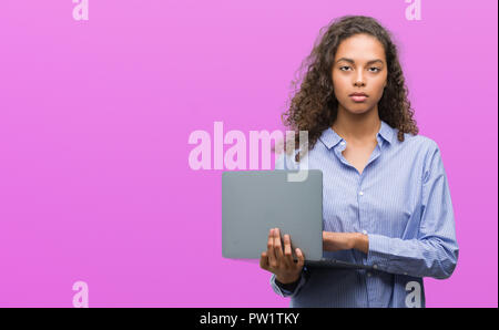 Young hispanic woman holding ordinateur portable avec une expression confiante face à la pensée intelligente grave Banque D'Images