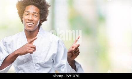 South American man wearing kimono karaté sur fond isolé en souriant et regardant la caméra pointant à deux mains et les doigts sur le côté. Banque D'Images