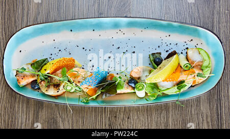 Rouleaux de poisson frit avec des herbes et légumes sur plaque bleue Banque D'Images