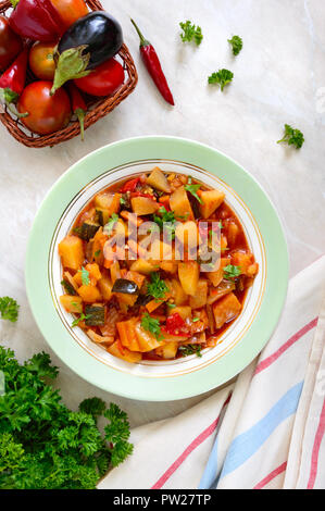 Délicieux Ragoût aux légumes dans un bol sur la table. Compote de pommes de terre, aubergines, courgettes, oignons, carottes en sauce tomate piquante avec les verts. Banque D'Images