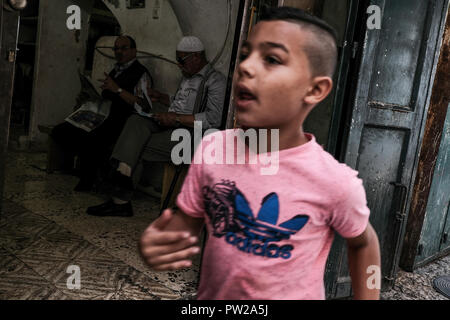 Jérusalem, Israël. 11 octobre, 2018. Un jeune garçon passe devant l'entrée d'une boutique de tailleur dans la vieille ville de Jérusalem le quartier musulman. Banque D'Images