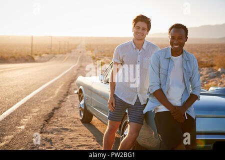 Portrait de deux amis profitant de Road Trip debout à côté de voiture de collection sur la route du désert Banque D'Images