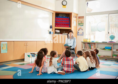 Les enfants à l'école assis sur le plancher réunis autour d'enseignant Banque D'Images