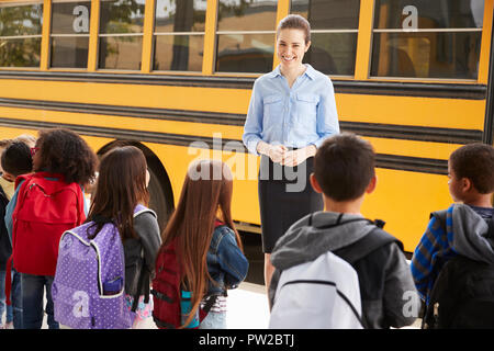 Parler de l'enseignant à l'école élémentaire les enfants par autobus scolaire Banque D'Images