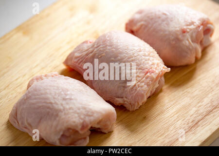 Trois cuisses de poulet cru acheté dans un supermarché au Royaume-Uni affiche sur une planche à découper en bois. Dorset England UK GO Banque D'Images