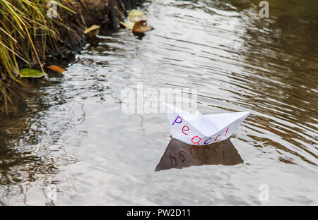 Papier blanc solitaire appelé bateau flottant sur un ruisseau de paix outdoor le sombre jour d'automne closeup Banque D'Images