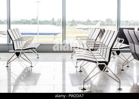 Chaises modernes en salle d'attente à l'aéroport avec des avions derrière la fenêtre Banque D'Images