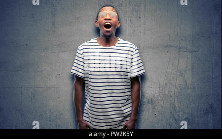 L'homme noir africain portant des lunettes de stressant, terrifiée, en panique, des cris exaspérés et déçus. Geste désagréable. Travail ennuyeux me c Banque D'Images