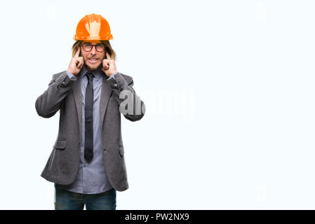 Beau jeune homme architecturaux aux cheveux longs portant un casque de sécurité sur fond isolé couvrant les oreilles avec les doigts avec l'expression ennuyé pour la n Banque D'Images