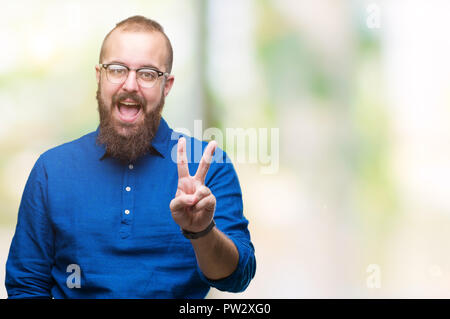 Hipster Young caucasian man wearing glasses sur fond isolé avec sourire heureux face à l'appareil photo faisant un clin la victoire. Numéro deux. Banque D'Images