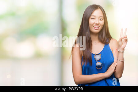 Young Asian Woman sur fond isolé avec sourire heureux face à l'appareil photo faisant un clin la victoire. Numéro deux. Banque D'Images