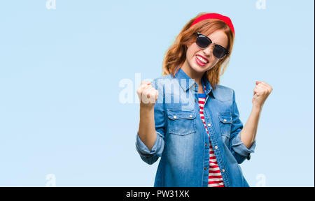 Belle jeune femme de plus fond isolé portant des lunettes de soleil très heureux et excité de faire geste gagnant avec bras levés, sourire et crier Banque D'Images