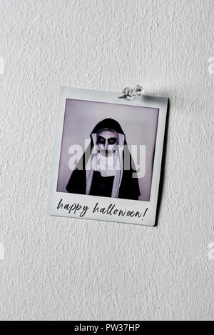 Une photo d'un mal effrayant nun, vêtu d'un habit noir et blanc typique, avec le texte happy Halloween écrit en C, épinglé à un mur blanc avec Banque D'Images
