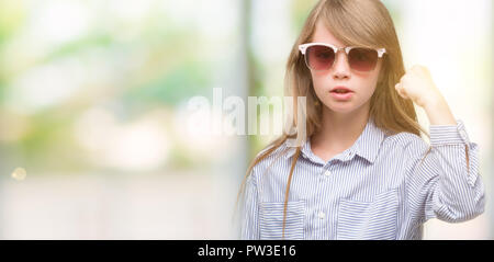 Jeune blonde toddler wearing blue shirt contrarié et frustré de crier avec colère, fou et hurlant de main levée, la colère concept Banque D'Images