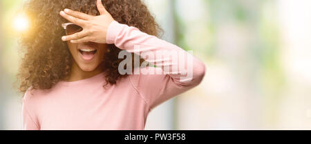 African American Woman wearing orange sunglasses peeking sous le choc couvrant le visage et les yeux avec la main, regardant à travers les doigts avec embarrassé d'expression. Banque D'Images