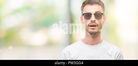 Les jeunes adultes portant des lunettes homme tatoué de peur face à une surprise de choc, de peur et d'excité avec crainte expression Banque D'Images