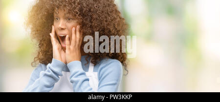 African American boutique femme portant un tablier stressant laissant les mains sur la tête, terrifié, criant en panique Banque D'Images