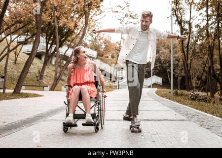 L'homme excité équitation skateboard et mobilité petite amie en souriant Banque D'Images