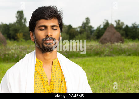 Personne mâle indien ou yogi close-up de calme expression avec les yeux fermés des vêtements blancs sur chemise jaune avec fond naturel Banque D'Images