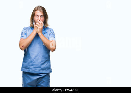 Beau jeune homme médecin aux cheveux longs sur fond isolé choqué couvrant la bouche avec les mains pour l'erreur. Concept Secret. Banque D'Images