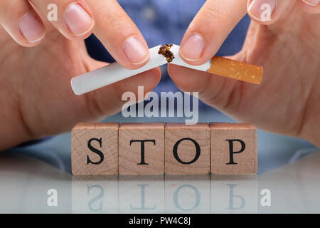 Woman's Hand Breaking Cigarette arrêter sur des blocs de bois on Reflective 24 Banque D'Images