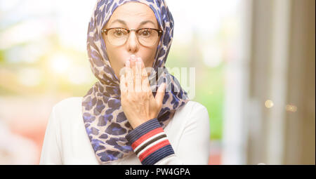 L'âge moyen arabe musulmane woman wearing hijab couvre la bouche sous le choc, l'air timide, exprimant le silence et l'erreur, peur des concepts Banque D'Images