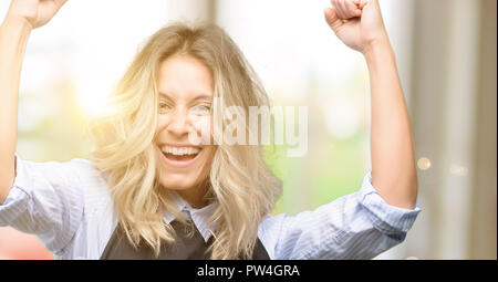 Jeune propriétaire de boutique Portant tablier noir heureux et excité célébrant la victoire l'expression de grand succès, la puissance, l'énergie et des émotions positives. Célèbre De nouveaux Banque D'Images