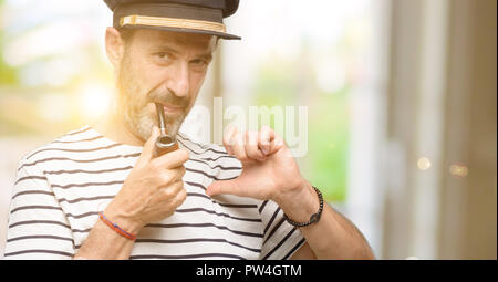 Le capitaine marin homme fumer une pipe fier, heureux et fier, en pointant avec la victoire face à Banque D'Images