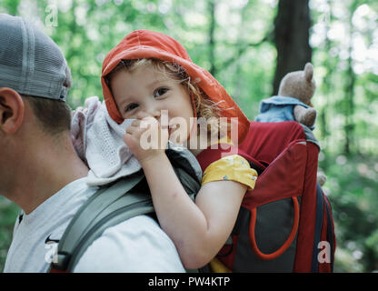 Portrait of cute fille heureuse la succion du pouce alors qu'ils étaient acheminés par le père dans la forêt Banque D'Images
