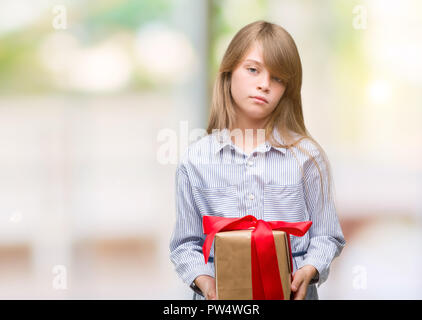 Jeune blonde enfant tenant un présent avec une expression confiante face à la pensée intelligente grave Banque D'Images