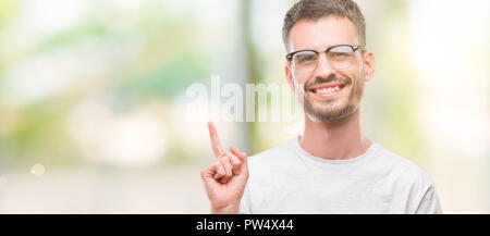 Les jeunes adultes tatoués homme avec un grand sourire sur le visage, en pointant avec la main et le doigt sur le côté regardant la caméra. Banque D'Images