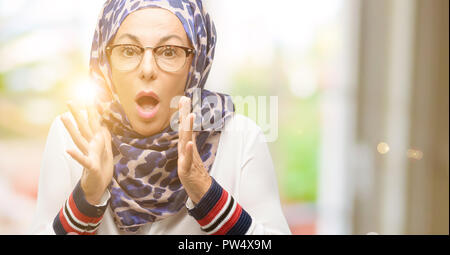 L'âge moyen arabe musulmane woman wearing hijab stressant en gardant les mains sur la tête, terrifié, criant en panique Banque D'Images