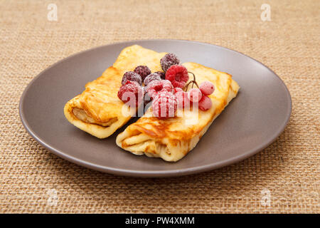 Crêpes maison remplie de fromage cottage et garnie de framboises congelées et les mûres sur la plaque et des sacs sur arrière-plan Banque D'Images