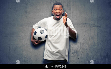 African black man holding soccer ball stressant en gardant les mains sur la tête, terrifié, criant en panique Banque D'Images