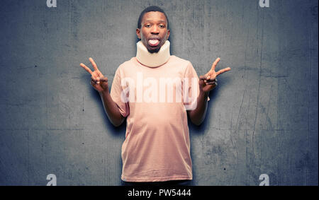 Homme noir africain blessés wearing neck brace à la caméra en montrant tong et faire de la victoire avec les doigts Banque D'Images