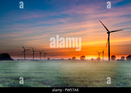 Éoliennes dans le domaine dramatique avec brouillard ciel coucher de soleil coloré. Source d'énergie durable concept abstrait. Banque D'Images