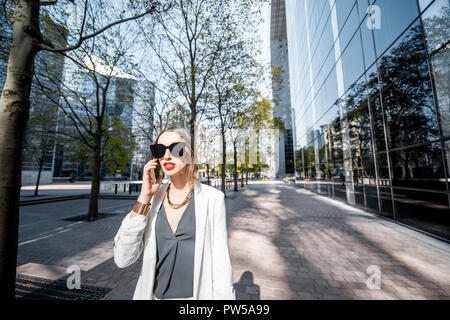 Portrait de vie d'une femme d'affaires en costume blanc avec le smartphone au quartier financier avec les bâtiments modernes sur l'arrière-plan Banque D'Images