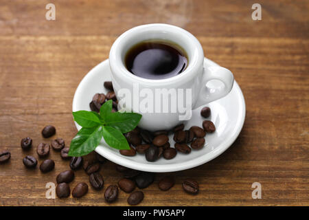 Une tasse de café noir avec des grains de café torréfié et de feuilles sur fond blanc Banque D'Images