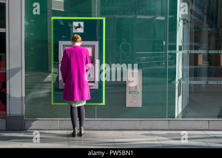 Femme portant une robe rose à un distributeur automatique de la Banque Lloyds. London, UK Banque D'Images