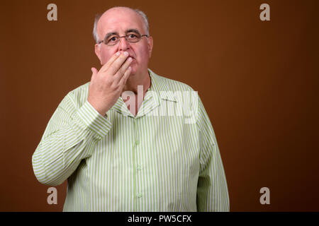 L'embonpoint senior man wearing eyeglasses contre brown backgroun Banque D'Images