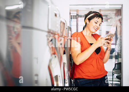 Happy caucasian middle age dame utiliser smart mobile phone au lavoir automatique mat service shop tout en attendre ses vêtements lavés et propres Banque D'Images