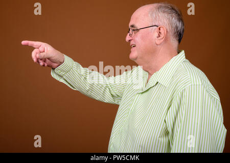 L'embonpoint senior man wearing eyeglasses contre brown backgroun Banque D'Images