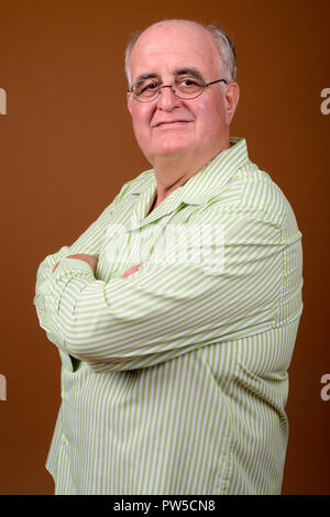 L'embonpoint senior man wearing eyeglasses contre brown backgroun Banque D'Images